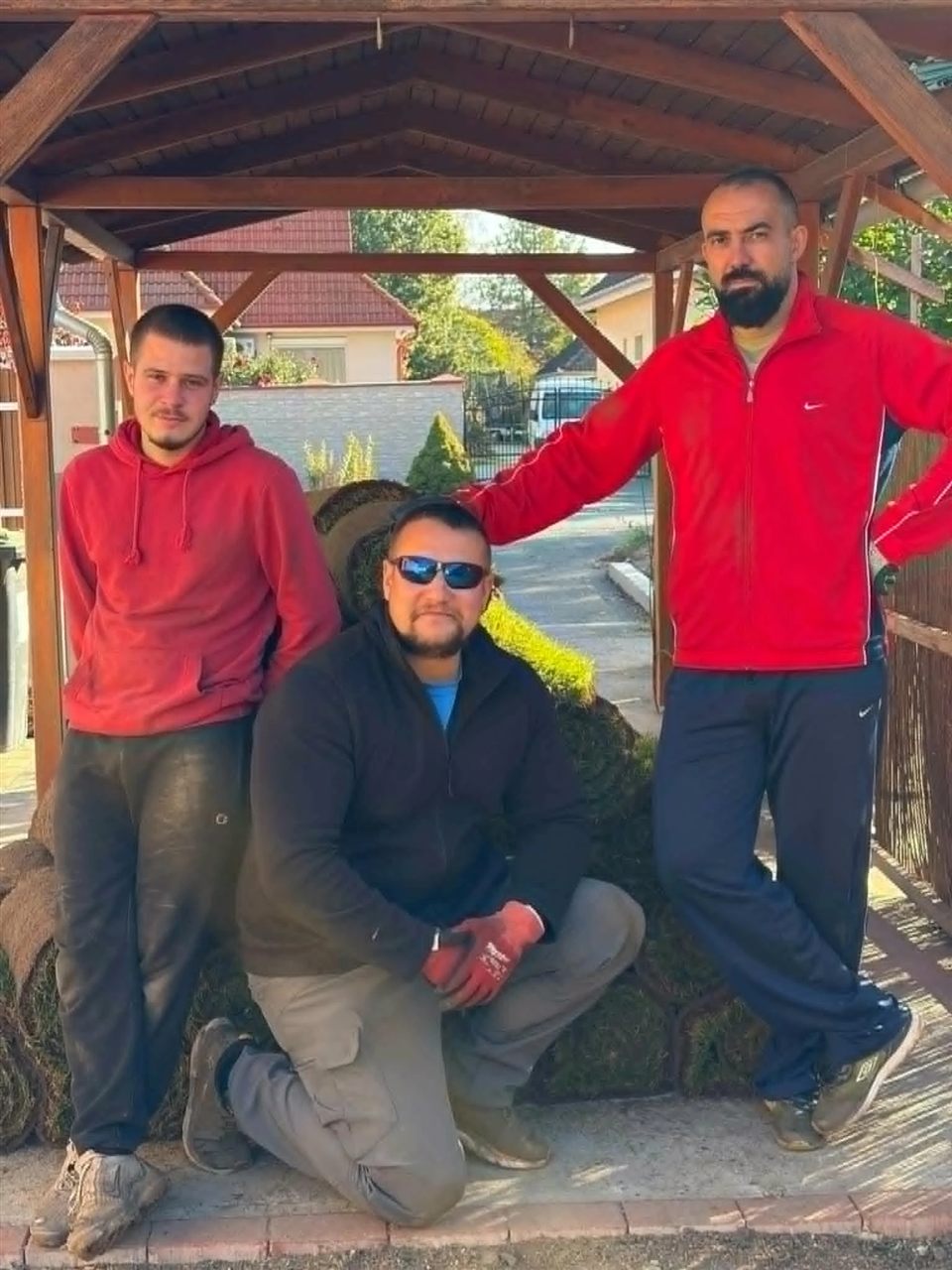 A Gardenfix csapata: három kertész gyepszőnyeg-tekercsek előtt, egy kerti pavilon alatt