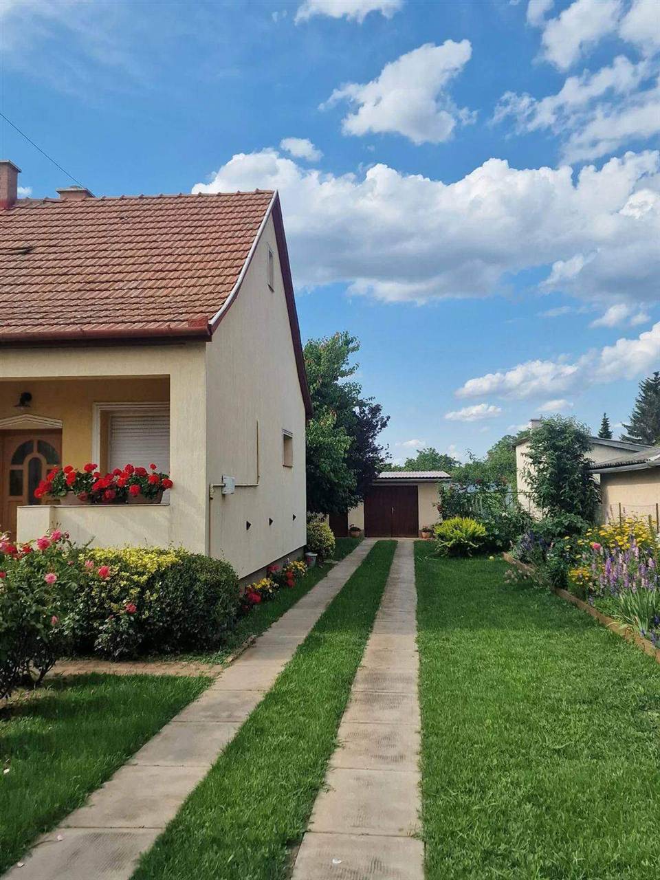 Térkővel szegélyezett gyalogút virágzó ágyások között a ház mellett